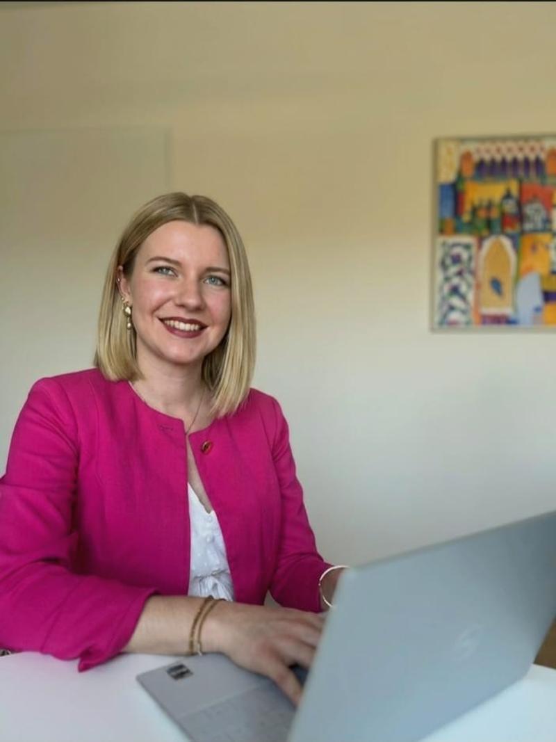 Julia Pashchenko im pinken Blazer an ihrem Schreibtisch